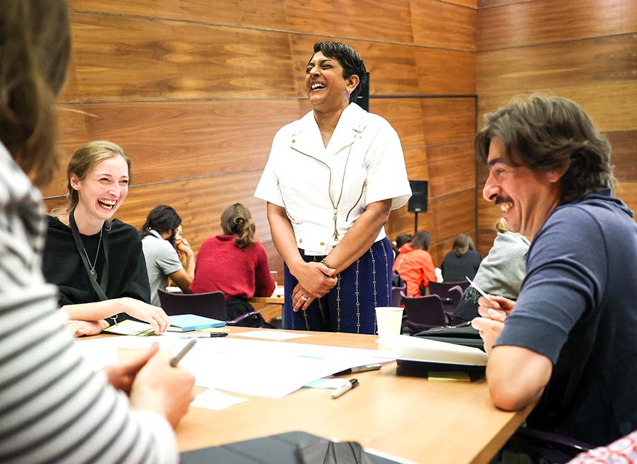 Attendees and speaker Meena Kothandaraman laughing around a workshop table.